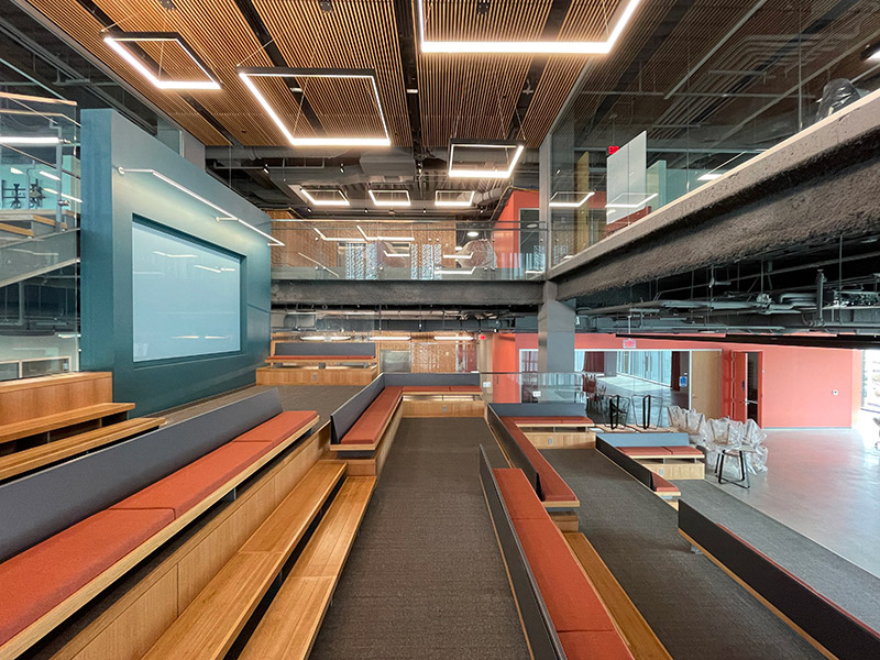 Modern collaborative forum space with tiered seating, open ceilings, and architectural LED lighting at the University of Delaware FinTech Innovation Hub renovation