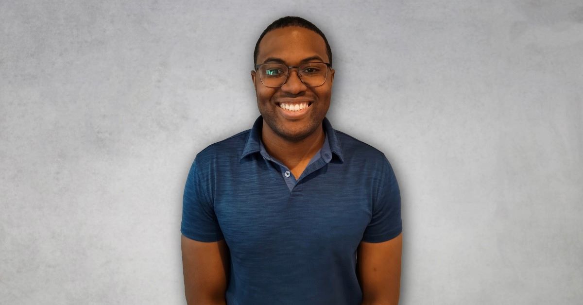Ethan Brown smiling in a professional headshot, wearing glasses and a navy-blue polo shirt against a light gray background.