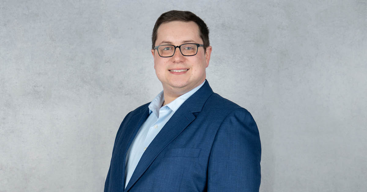 Michael Duffy, professional headshot, wearing a blue suit and glasses against a gray background.