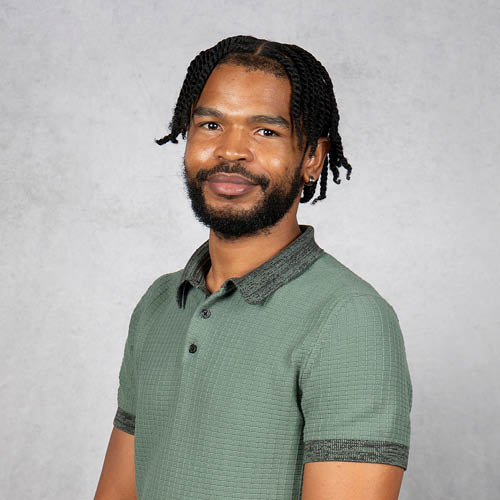 Professional headshot of Okein Miller wearing a green collared shirt, smiling against a gray studio background.
