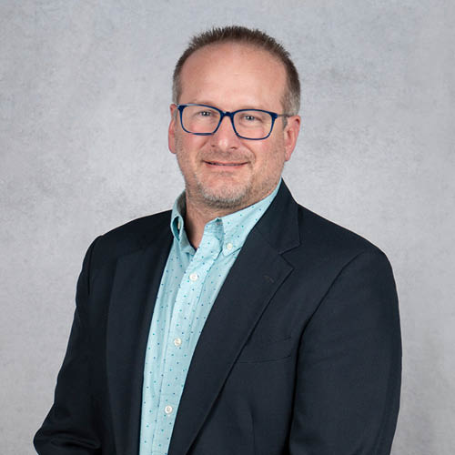 Shawn D. Good professional headshot wearing glasses, blazer, and button-down shirt against a neutral background.