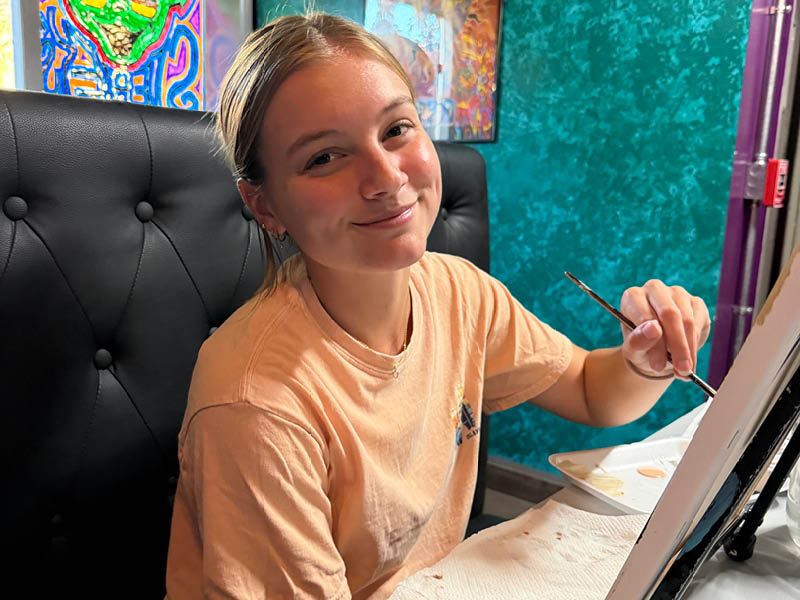Aubrey smiling while painting on a canvas at an art studio.