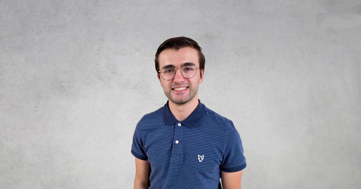 Professional headshot of Kohl H. Lindaman wearing glasses and a blue striped polo shirt against a gray background.