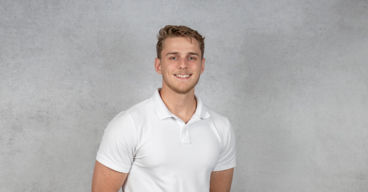 Professional headshot of Logan E. Keen wearing a white polo shirt, smiling against a light gray studio background.