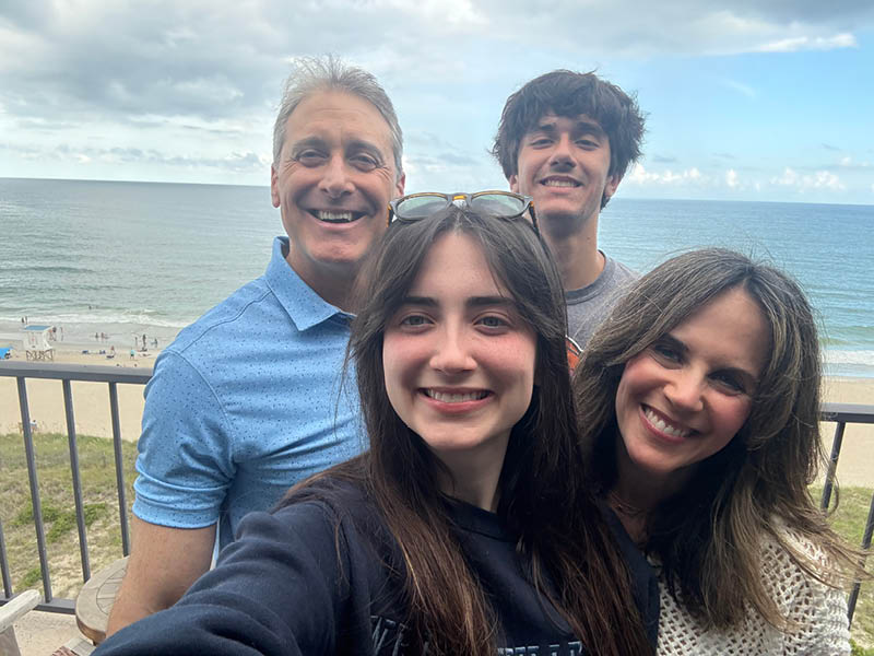 Ava smiling with family on a balcony overlooking the ocean during a beach vacation