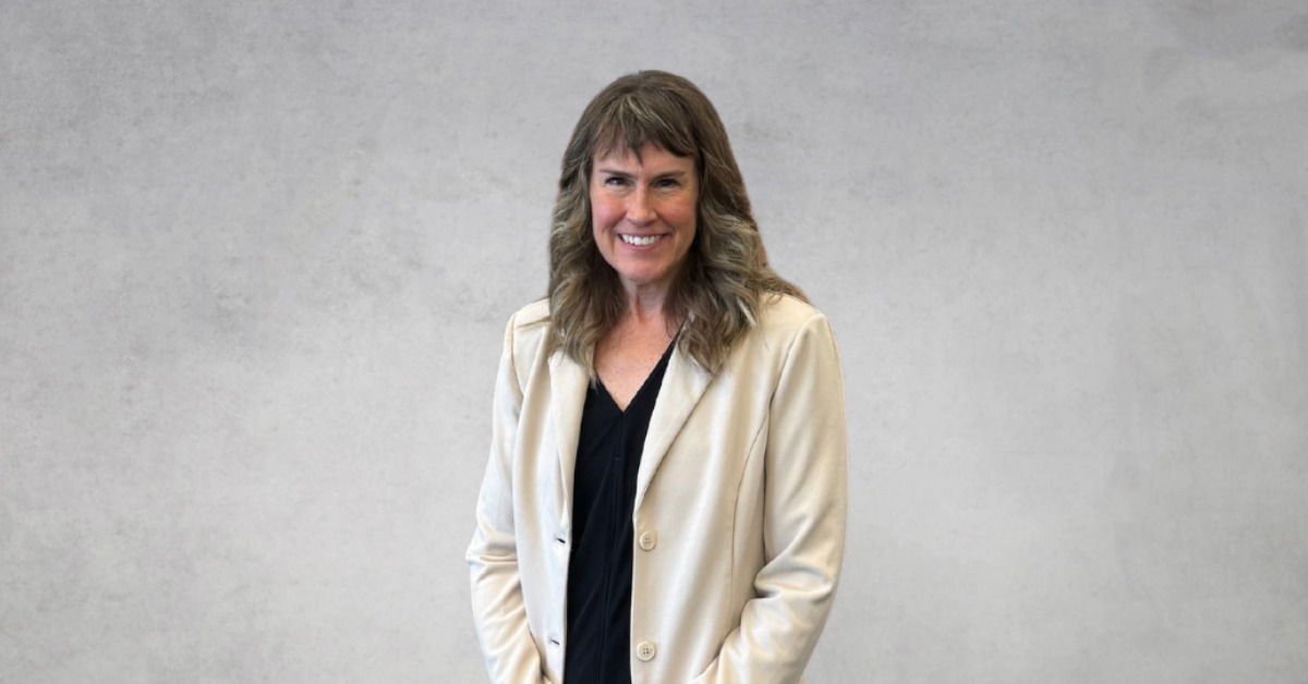 Jennifer L. Rager smiles for a professional headshot while wearing a cream blazer and black blouse against a neutral gray background.