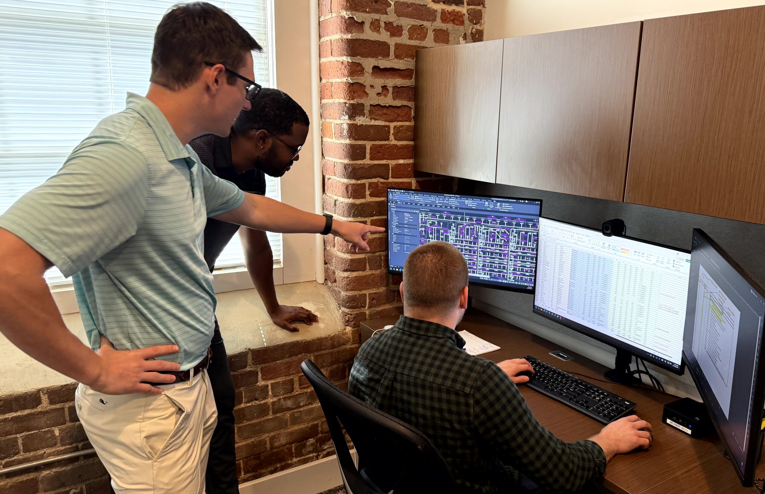 MEP engineers collaborate on building system plans and technical designs displayed on computer monitors.
