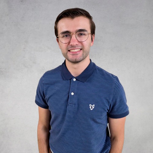 Kohl wearing glasses and a blue striped polo shirt smiling against a light gray background.
