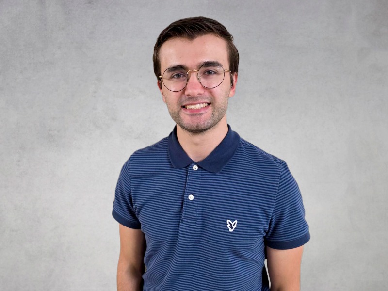 Kohl wearing glasses and a blue striped polo shirt smiling against a light gray background.