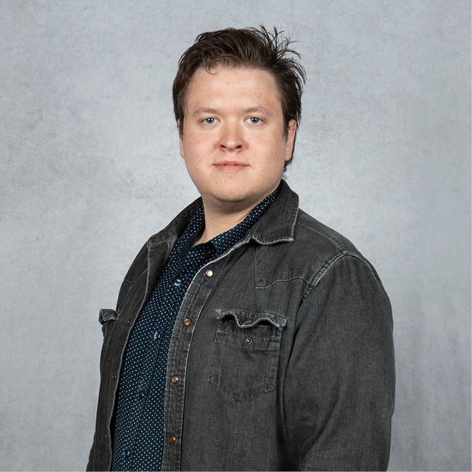 Samuel wearing a dark denim jacket over a patterned shirt against a light gray background.