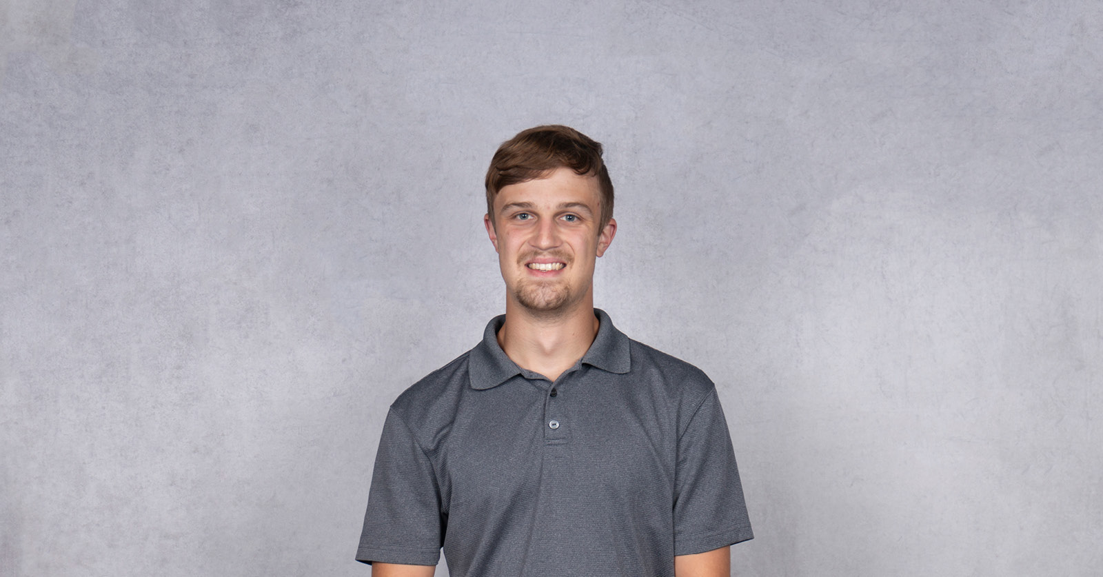 Professional headshot of Daniel wearing a gray polo shirt against a light gray background.