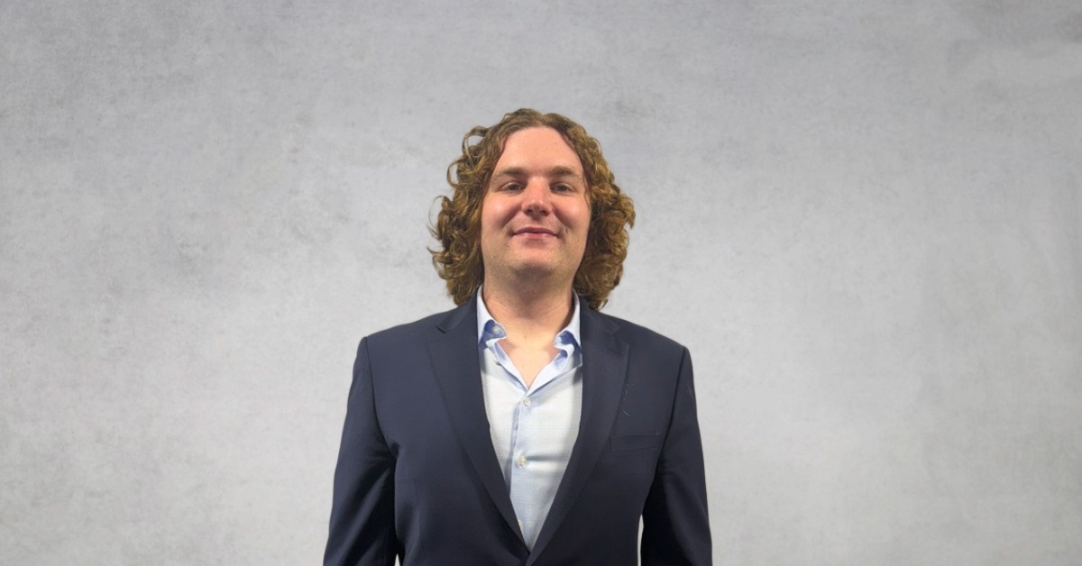 Professional headshot of a Declan wearing a navy blazer and light blue shirt against a neutral gray background.